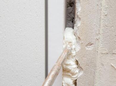 Close-up of expanding foam being injected into a gap between a door frame and wall structure using a foam gun, demonstrating Evostik filling and insulation solutions for sealing cavities and improving thermal efficiency.
