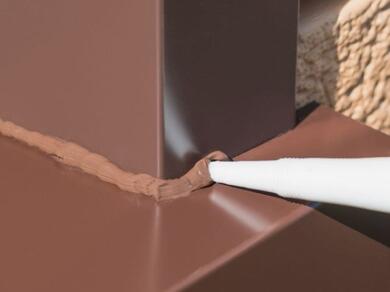 Close-up of Evostik Design Sealant being applied to a colour-matched corner joint around a coated metal frame, creating a neat, weatherproof seal between architectural metal surfaces.