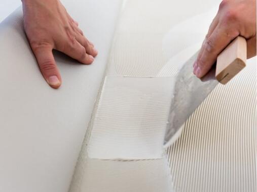 Close-up of a trowel applying and smoothing flooring adhesive on a textured subfloor, demonstrating floor preparation for adhesive installation.